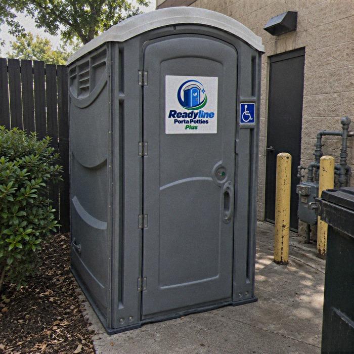 Wide grey ADA porta potty with wheelchair symbol beside a brick building