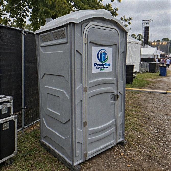 Grey porta potty on a grass path between temporary fences at a festival