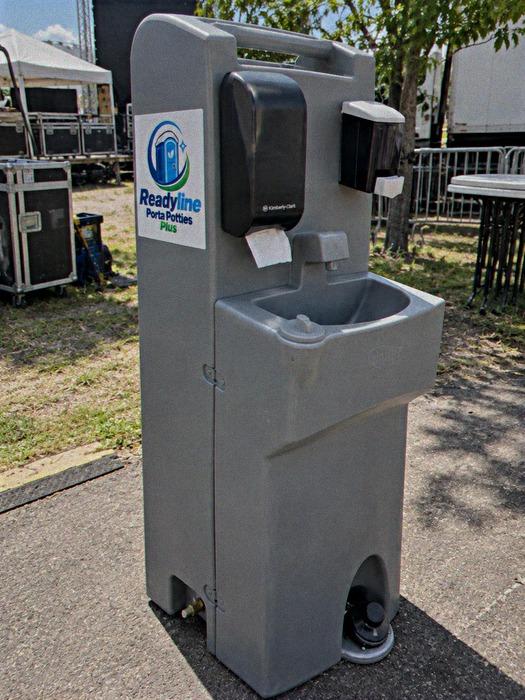 Grey freestanding hand-wash sink stand with soap and towel dispensers at an outdoor event