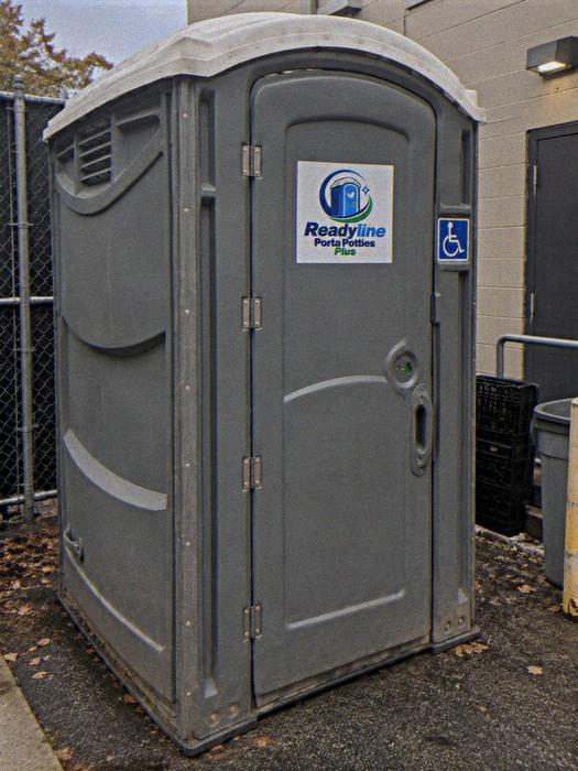 Grey accessible portable toilet with wheelchair decal in a back lot