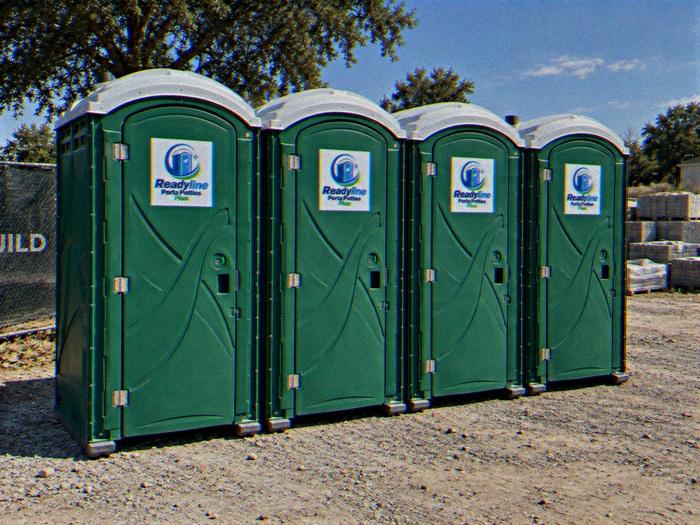Row of four green porta potty rental units on gravel in Raleigh